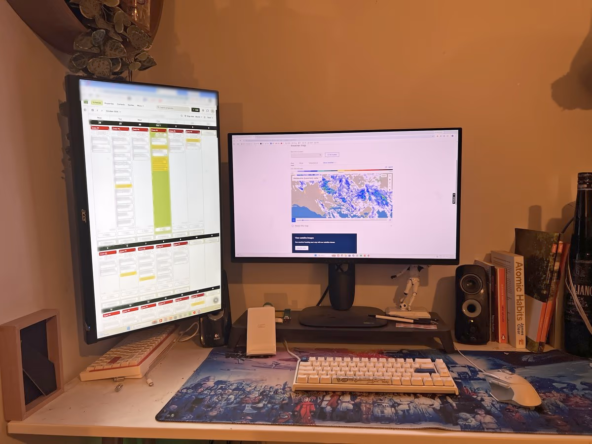Tim's desk in the evening: SortScape's month view on a portrait monitor, with customer details blurred, and a weather radar on the second screen