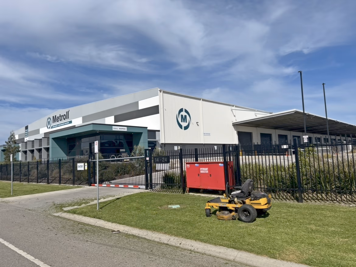 A zero-turn mower on the nature strip outside a fenced industrial site