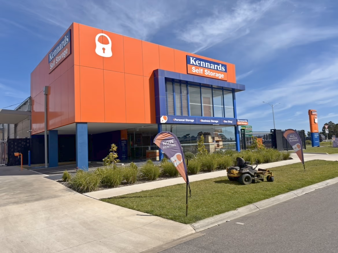 A zero-turn mower parked on the lawn strip outside a commercial building