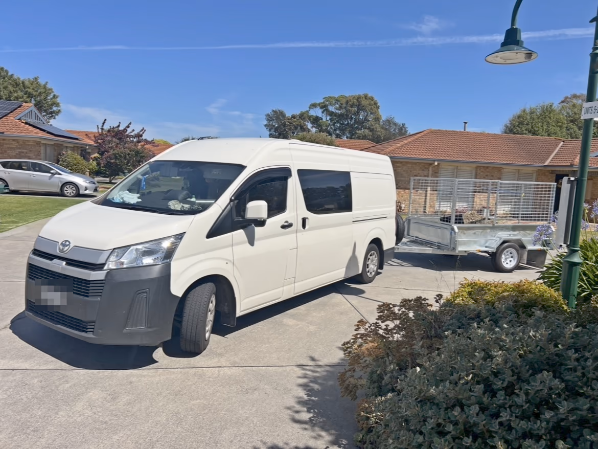 A white van towing a trailer parked in the driveway of a unit complex
